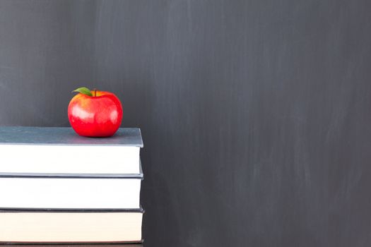 Stack of books with a red apple and a clean blackboard