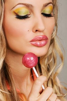 Young woman with vibrant makeup holding a red lollipop