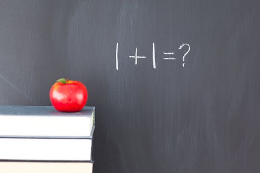 Stack of books with a red apple and a blackboard with "1+1=?" written on it