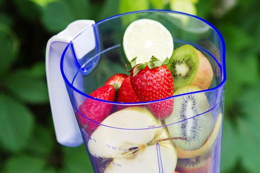 Electric blender with fruits in it, green leaves background