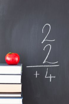 Stack of books with a red apple and a blackboard with a simple fraction written on it
