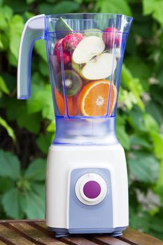 Electric blender with fruits in it, green leaves background