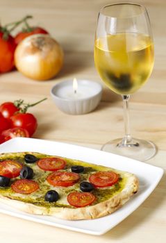 Pesto pizza with tomatoes and black olives on a white plate