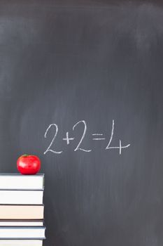 Stack of books with a red apple and a  blackboard with "2+2=4" written on it