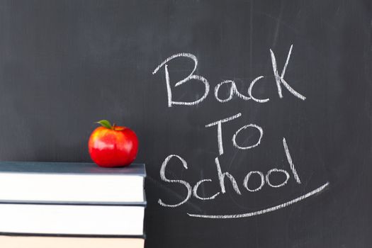 Stack of books with a red apple and a blackboard with "back to school" written on it