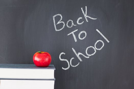 Stack of books with a red apple and a blackboard with "back to school" written on it