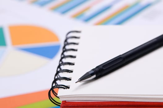 Close-up photo of a notebook and pen, with charts and diagrams on background