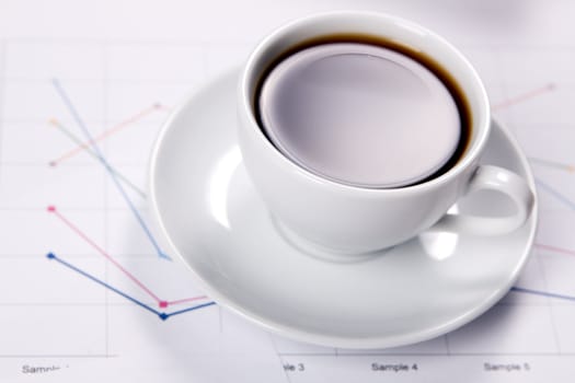 Cup of strong coffee over business diagrams, closeup soft focus photo