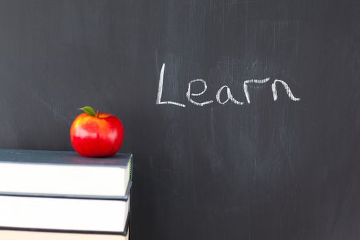 Stack of books with a red apple and a blackboard with "learn" written on it