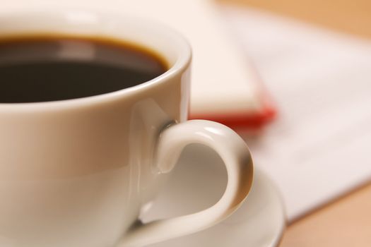 Worktable covered with documents, with a cup of coffee on foreground, soft focus