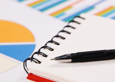 Close-up photo of a notebook and pen, with charts and diagrams on background