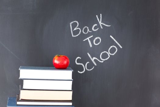 Stack of books with a red apple and a blackboard with "back to school" written on it