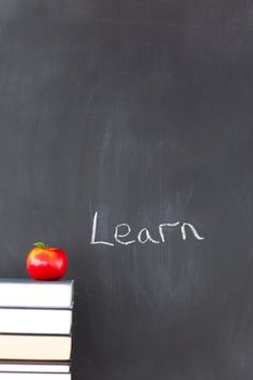 Stack of books with a red apple and a blackboard with "learn" written on it