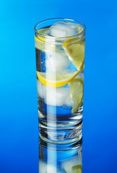 Glass of lemon ice water on blue background, studio photo