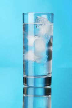 Glass of ice water on blue background, studio photo