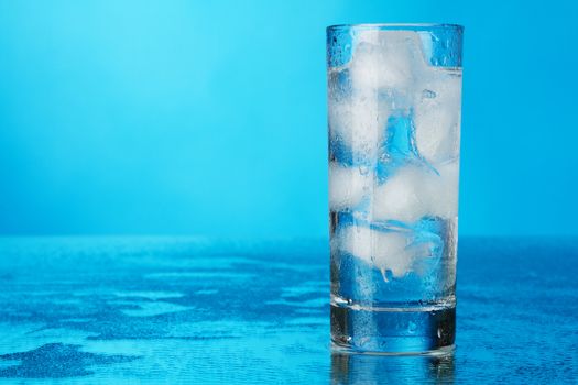 Glass of ice water on blue background, studio photo