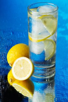 Glass of lemon ice water on blue background, studio photo