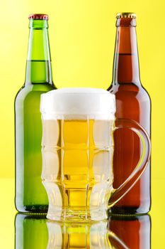 Beer mug and bottles on yellow background, studio photo