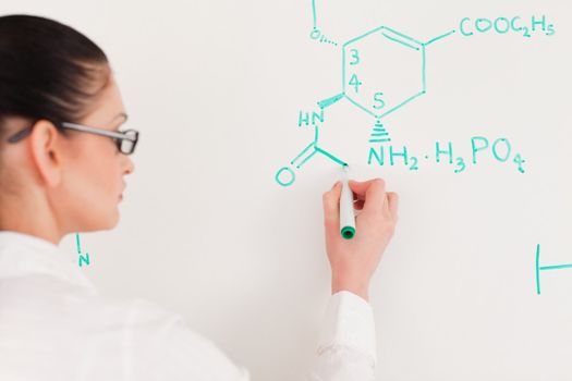 Dark-haired scientist woman writing a formula on a white board in a lab