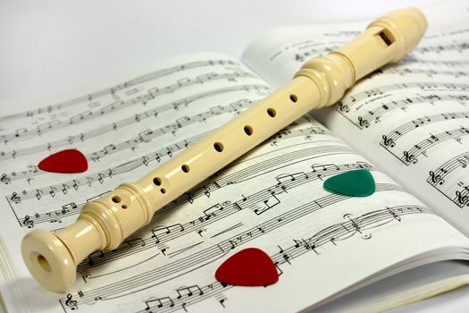 Flute (recorder) lying on notes sheet with several guitar pick-ups