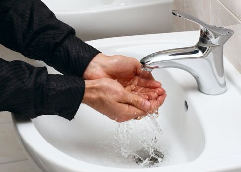Man washing his hands in running water, in a public toilet.
