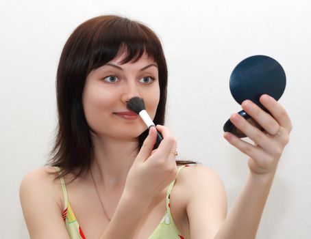 Beautiful girl making up, holding a powder brush and a mirror