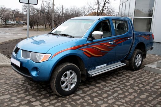 New blue pickup parked on stone pavement