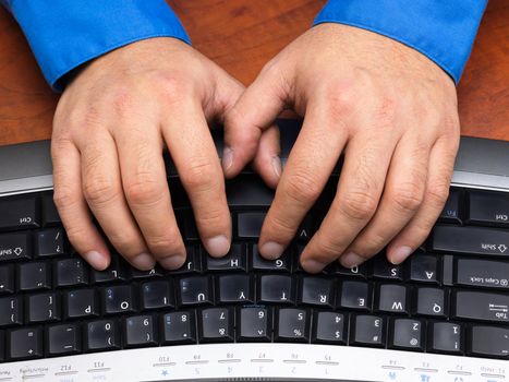 Close-up cropped shot of a human hands typing on black keyboard.