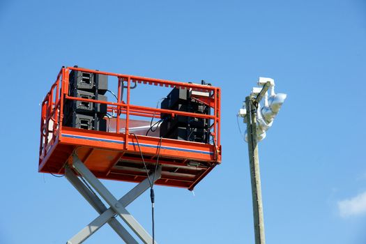 Stack of speaker equipment high in the sky on lift platform ready for outdoor concert in the park, beside lighting.