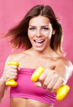 Beautiful slim woman with dumbbells, pink background