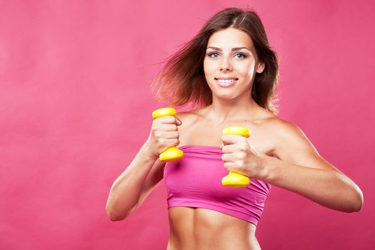 Beautiful slim woman with dumbbells, pink background