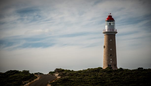 Winding road winds past a classic brick lighthouse with a traditional red and white top