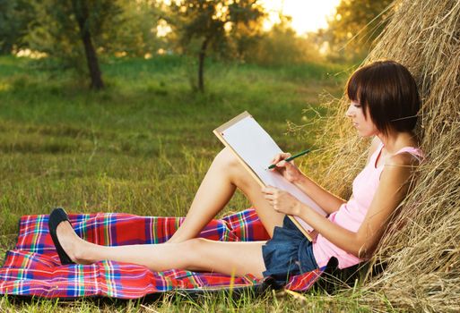 Lovely girl having rest and drawing in the park