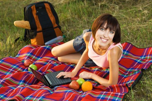 Lovely girl having a rest on picnic with laptop