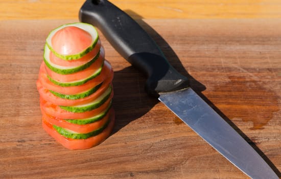 Pile of cut tomato cucumber slice and knife on wooden cutting board .