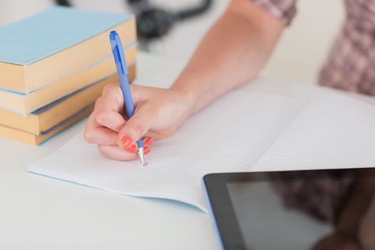 Woman writing on notepad with tablet pc in living room