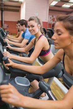 Smiling blonde on exercise bike in gym with other people
