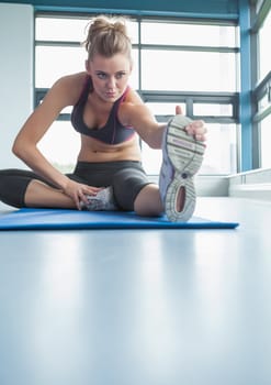 Sporty blonde stretching her leg in gym 