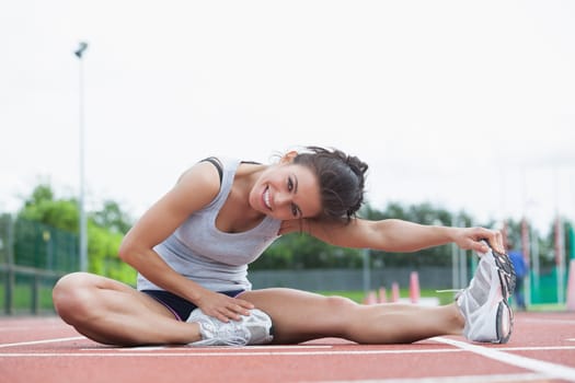 Smiling woman stretching her legs on a track