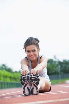 Smiling woman stretching legs on track 