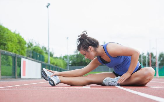 Woman stretching on a track in a stadium