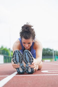 Woman stretching out on a track in a stadium