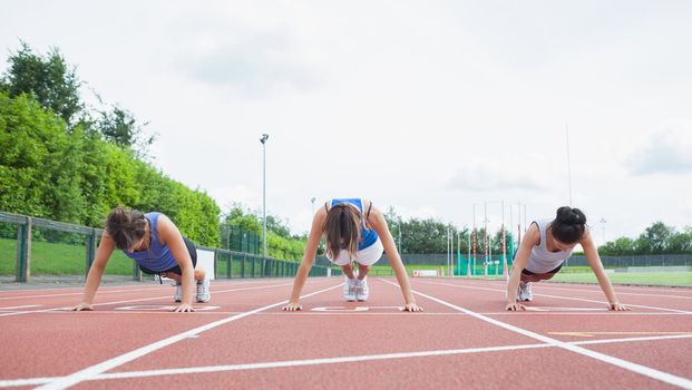 Three woman stretching on running track in stadium