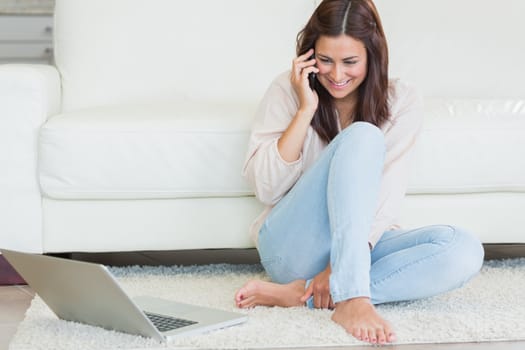 Woman calling in front of laptop on living room floor