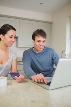 Two people sitting in the kitchen purchasing online on laptop in kitchen