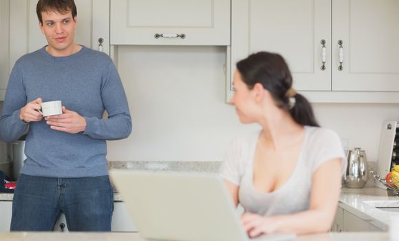 Two people spending time in the kitchen while using the laptop and drinking