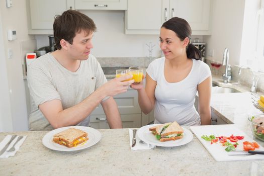 Two people eating sandwiches and drinking orange juice in the kitchen