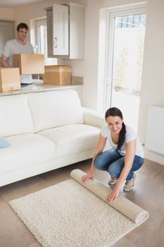 Two people furnishing the house while holding boxes and rolling out a carpet