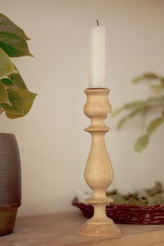Long white candle in a wooden candlestick on the shelf