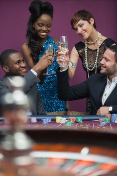 People clinking glasses at roulette table in casino